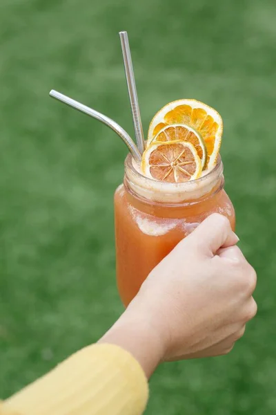 自然界のガラス瓶にレモンとオレンジのスライスとカクテルを保持する女性の垂直ショット — ストック写真