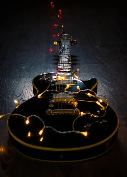 寄木細工の床の上のLedストリングライトに覆われた黒いエレキギターの垂直ショット — ストック写真