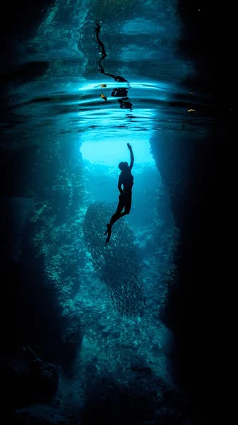 An underwater vertical shot of a diver reaching toward the surface with one hand-fantasy, mermaid concept