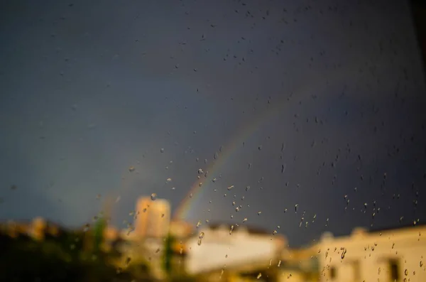 Egy Közeli Felvétel Egy Átlátszó Üvegről Esőcseppekkel Egy Város Szivárványának — Stock Fotó
