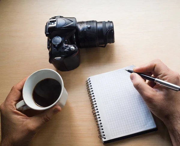 Fotógrafo Tomando Notas Enquanto Bebe Café Com Uma Câmera Mesa — Fotografia de Stock