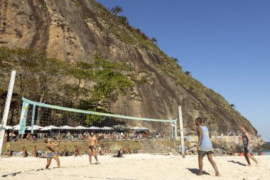 RIO DE JANEIRO, BRAZIL - Jul 19, 2020: Foot volleyball with volley net with one woman and two men playing in front of the Leme hill at the end of Copacabana boulevard clipart