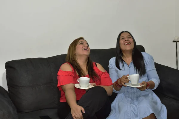两个女性朋友坐在沙发上 一边笑一边喝咖啡 — 图库照片