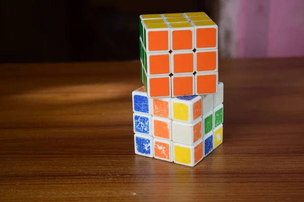 A closeup of a solved Rubik\'s cube on an unsolved cube on the table with a blurry background