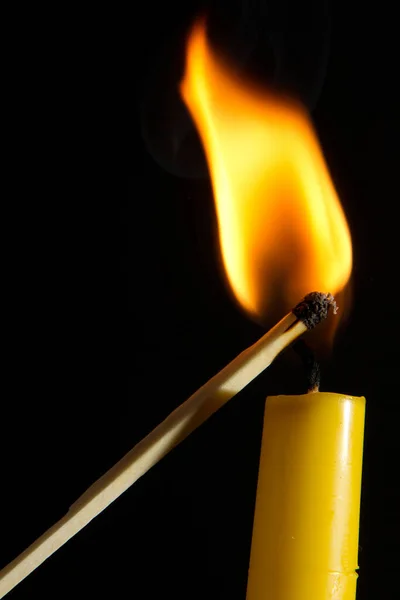 A vertical shot of a match lighting a candle isolated on a black background