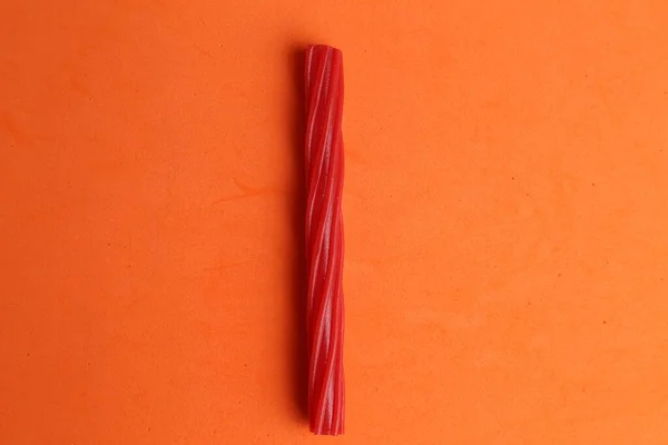 A closeup shot of a red licorice candy on an orange background