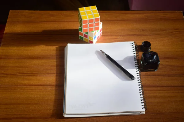 在一张桌子上有一个装有记事本和一支墨水笔的解决了的和未解决的Rubik立方体的高角视图 — 图库照片