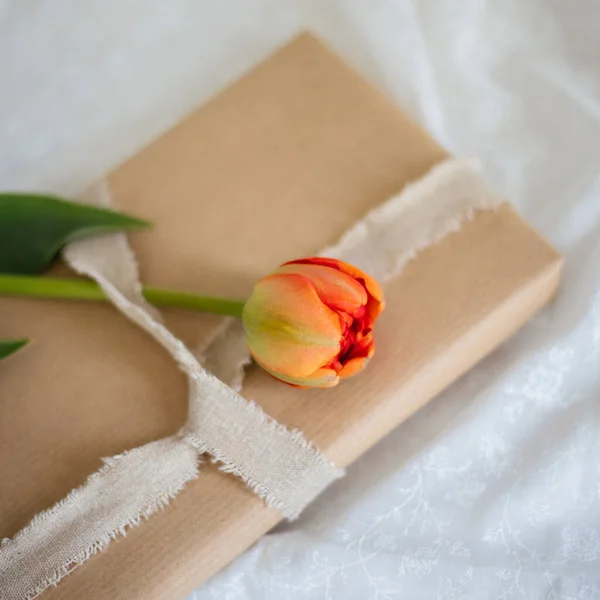 Miękkie Skupienie Prezentu Owiniętego Brązowym Papierem Białą Tasiemką Pomarańczowym Kwiatem — Zdjęcie stockowe