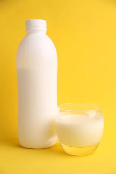 Λευκό Πλαστικό Μπουκάλι Δίπλα Στο Ποτήρι Του Χυμού Στο Κίτρινο — Φωτογραφία Αρχείου