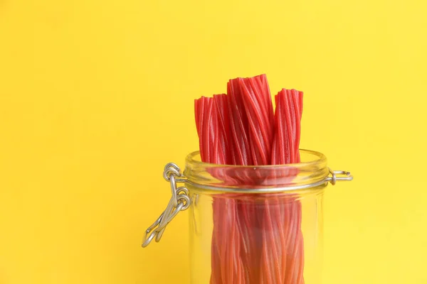 A closeup shot of red licorice sticks in the jar on a yellow background