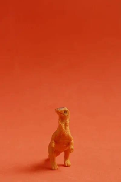 Pionowe Ujęcie Zbliżeniowe Gumowej Zabawki Kształcie Dinozaura Pomarańczowym Tle — Zdjęcie stockowe