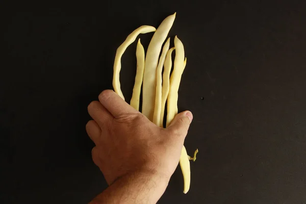 Eine Männliche Hand Legt Gelbe Spargelbohnen Auf Eine Schwarze Oberfläche — Stockfoto