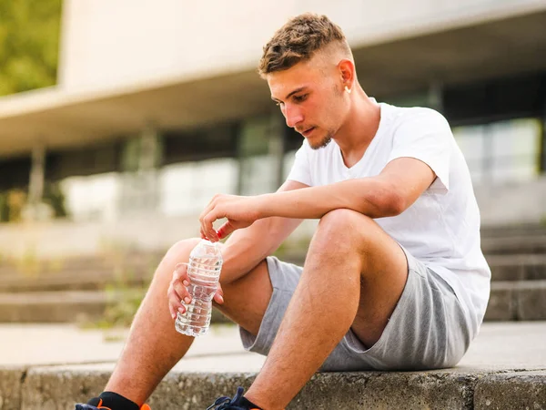 A shallow focus shot of a Caucasian male drinking water after a workout in a park