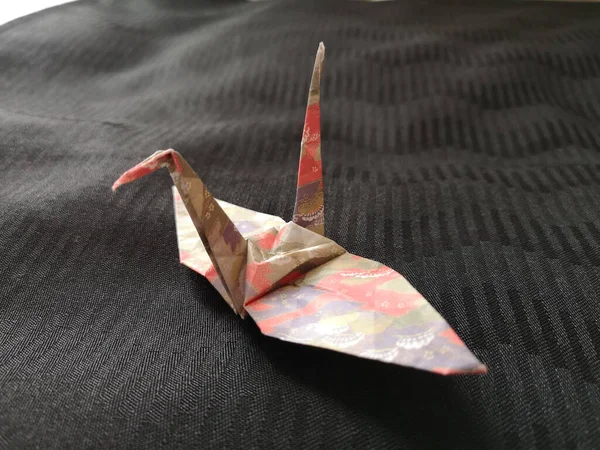 A closeup shot of an origami bird on a black textile