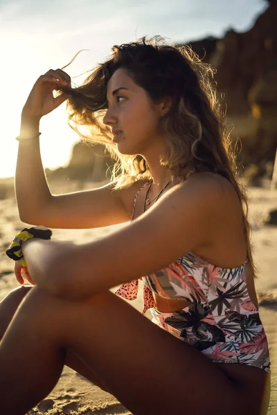 太陽の光を背景に砂浜に座っている水着の女性の垂直ショット — ストック写真