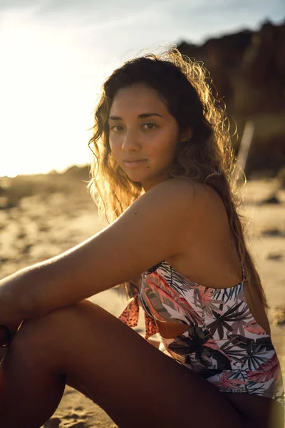 太陽の光を背景に砂浜に座っている水着の女性の垂直ショット — ストック写真