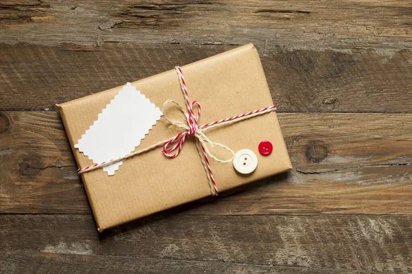 用褐色的纸和红丝带包裹在木制背景上的礼物的头像 — 图库照片