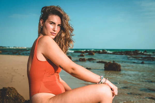 一个漂亮的欧洲女人穿着橙色泳衣坐在海滩上 — 图库照片