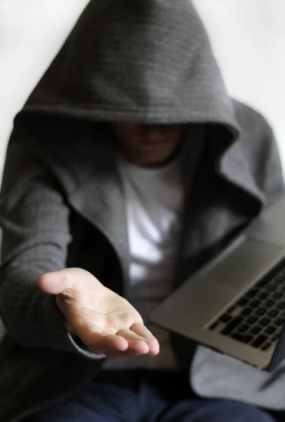 Eine vertikale Aufnahme eines vermummten Mannes in der Nähe eines Laptops, der seine Hand außerhalb des Cybersicherheitskonzepts hält — Stockbild Eine Vertikale Aufnahme Eines Vermummten Mannes Der Nähe Eines Laptops — Stockfoto