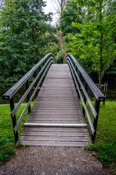 昼間に緑に覆われた公園内の小さな川に架かる橋の垂直ショット — ストック写真