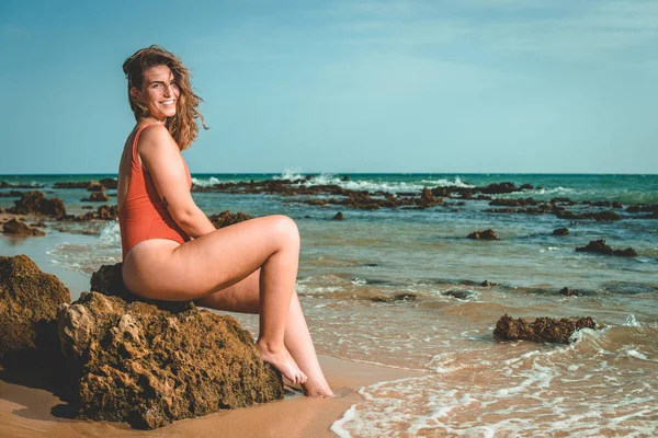 一个漂亮的欧洲女人穿着橙色泳衣坐在海滩上 — 图库照片