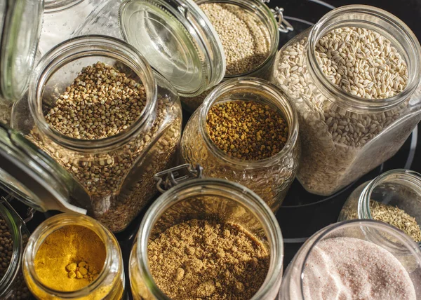 A close up shot of transparent jars of oats, salt, lentils, honey, rice, turmeric and panela