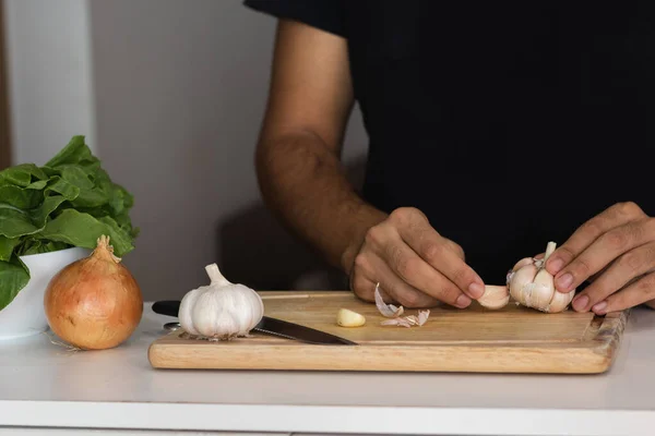 A closeup shot of a cutting board and a young man cutting garlic