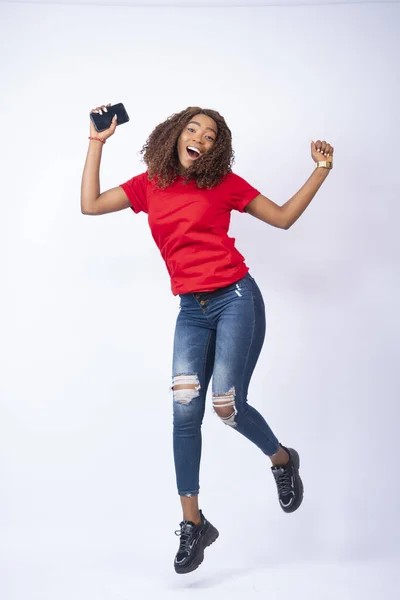 一个年轻快乐的黑人女士兴奋地跳起来拿着电话的垂直镜头 — 图库照片
