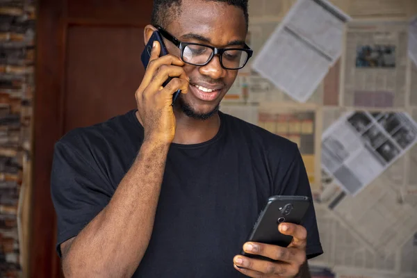 部屋で別の男を使用している間 電話で話しているメガネを持つ若いアフリカの男性 — ストック写真
