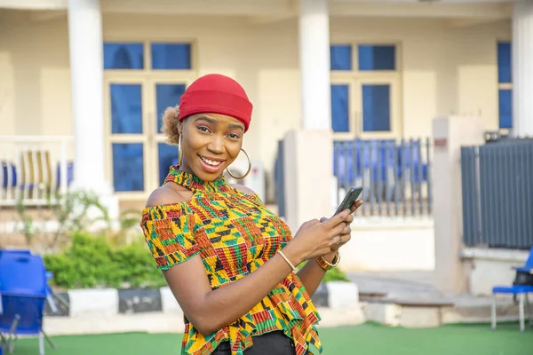 一个年轻漂亮的非洲女人笑着在外面用她的手机 — 图库照片
