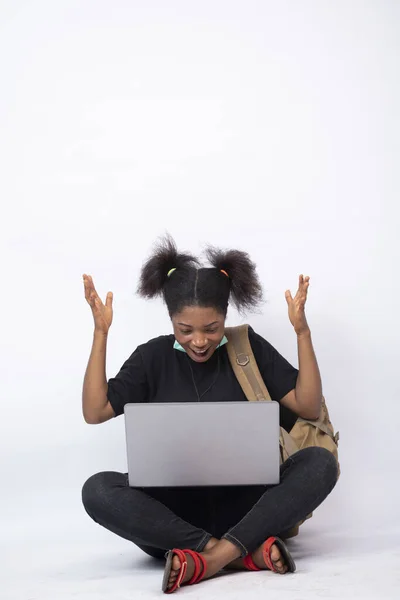 一个拿着背包的兴奋的非洲女人用笔记本电脑跨坐着庆祝 — 图库照片