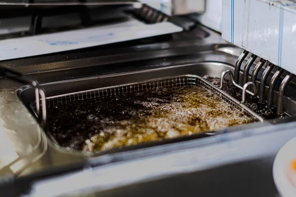 A high angle shot of french fries being fried in a lot of oil in the kitchen