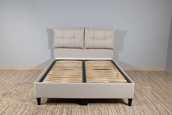 A bed with creme upholstery and wooden storage, without mattress