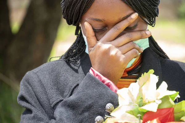 A young black woman mourning, wearing a mask and holding flowers - the new normal concept