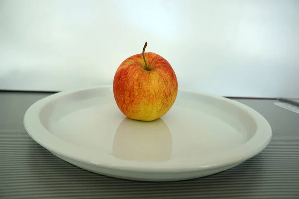 Ein Rot Gelber Apfel Auf Einem Weißen Teller — Stockfoto