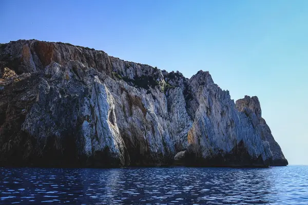 大海的波浪被蓝色天空下闪烁着光芒的岩石悬崖峭壁所环绕 这对墙纸来说真是太棒了 — 图库照片