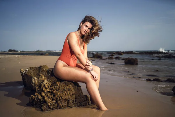 在一个刮风的日子里 一个漂亮的女人坐在西班牙罗塔海滩的岩石上 — 图库照片