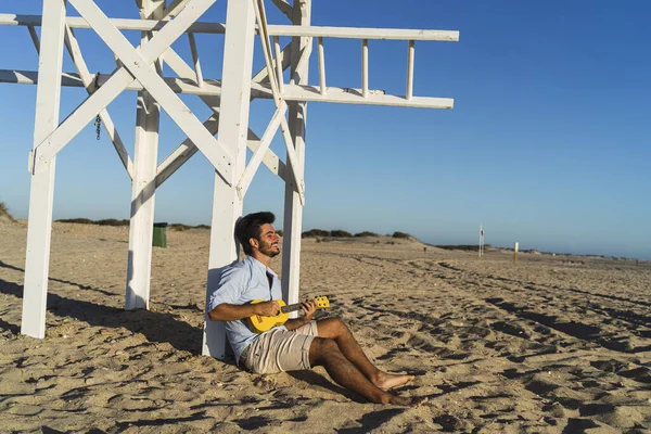 Młody Mężczyzna Grający Ukulele Siedzący Pod Drewnianą Konstrukcją Plaży San — Zdjęcie stockowe