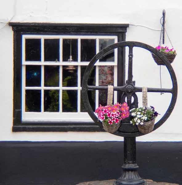 stock image A closeup of a decorative iron steering wheel with hanging potted flowering plants and a window in the background