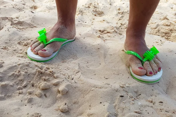 A closeup of female feet in sandals on a sandy beach