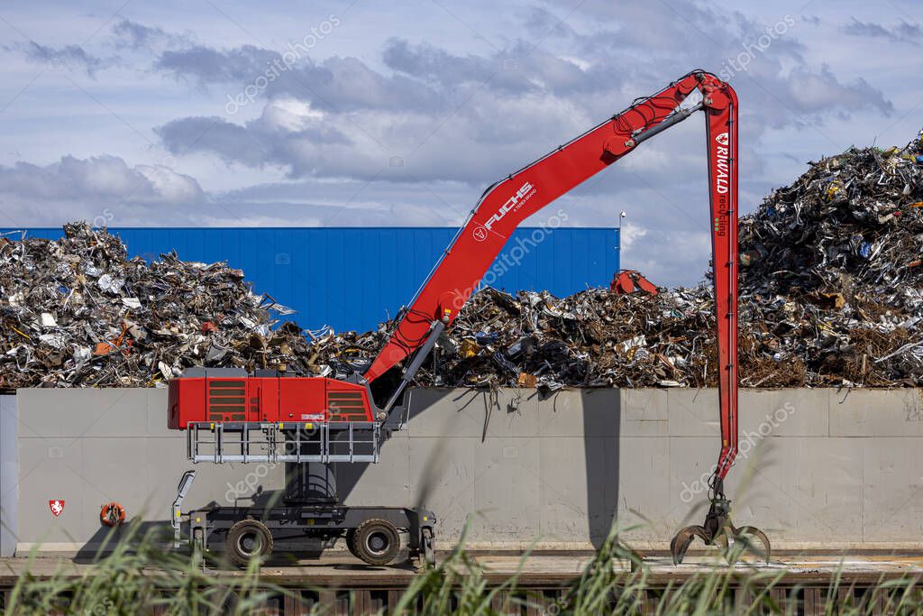 ALMELO, NETHERLANDS - Jul 27, 2020: Loading and unloading crane at Riwald recycling metal junkyard with the Twentekanaal river in the foreground against an overcast sky