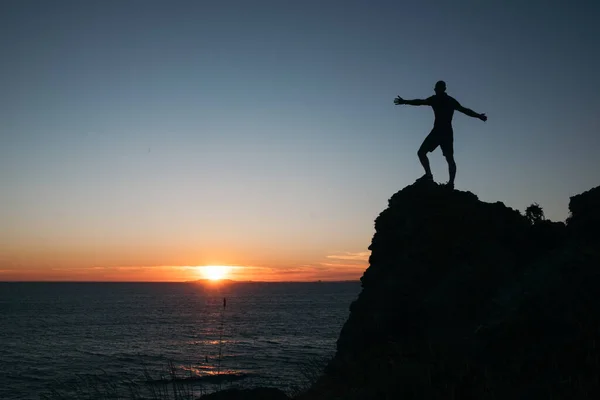 A silhouette of a person standing on a rock with arms spread out - freedom concept