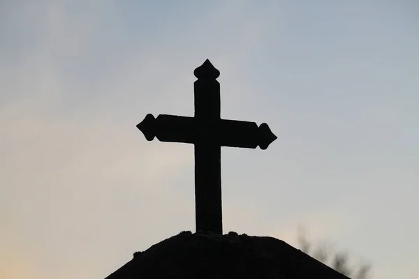 A dark cross from the entrance of a cemetery