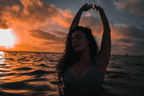 Kręcone Brunetka Kobieta Pozowanie Oceanie Pod Zachmurzonym Słońcem Niebo — Zdjęcie stockowe
