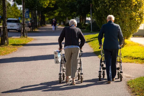 Two old people with Rollator Walkers in a park under the sunlight at daytime