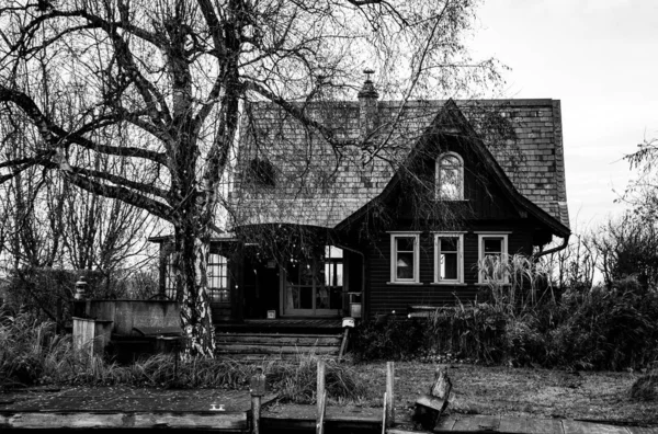 芝生の上に乾燥した死んだ植物と古い放棄された家の灰色スケールの劇的なショット 狩猟家の概念 — ストック写真