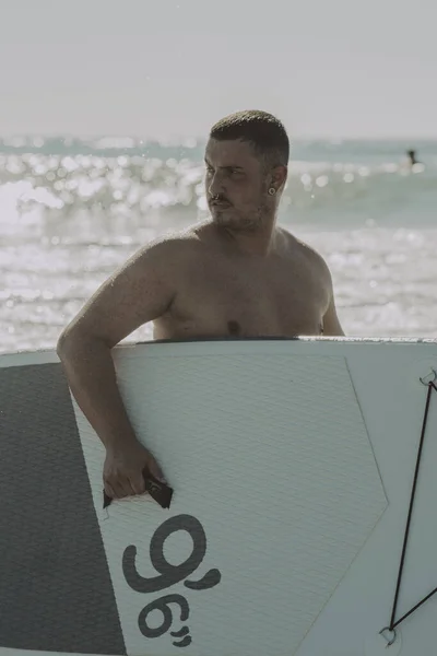 Pionowe Ujęcie Młodego Człowieka Oceanie Trzymającego Deskę Surfingową — Zdjęcie stockowe