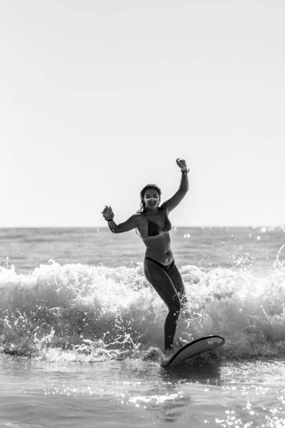 水中のサーフィンボード上の美しい若い女性のグレースケールショット — ストック写真