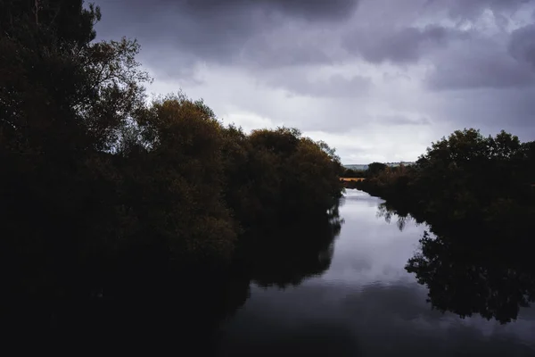 Una Silhouette Alberi Accanto Fiume Con Uno Sfondo Nuvoloso Tempestoso — Foto Stock