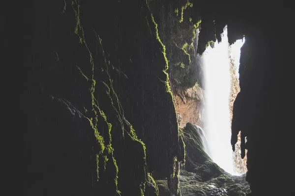 从漆黑的苔藓洞穴中俯瞰瀑布的迷人景象 — 图库照片